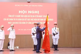 Tổng Bí thư Tô Lâm gắn huy hiệu “Anh hùng lực lượng vũ trang nhân dân” lên lá cờ truyền thống của Cục An ninh mạng và phòng, chống tội phạm sử dụng công nghệ cao, Bộ Công an. (Ảnh: Phạm Kiên/TTXVN)