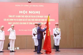 Tổng Bí thư Tô Lâm gắn huy hiệu “Anh hùng lực lượng vũ trang nhân dân” lên lá cờ truyền thống của Cục An ninh mạng và phòng, chống tội phạm sử dụng công nghệ cao, Bộ Công an. (Ảnh: Phạm Kiên/TTXVN)