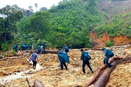 Bộ đội chi làm nhiều nhóm đi bộ vượt các điểm sạt lở, đường núi và sông suối gùi nhu yếu phẩm đến 14 hộ dân bị cô lập. (Ảnh: PV/Vietnam+)