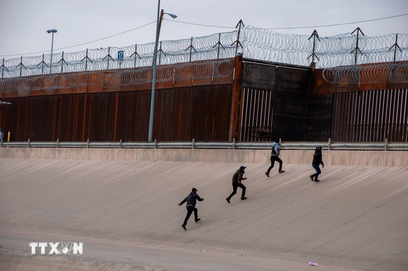 Những người di cư chuẩn bị vượt qua bức tường biên giới Mỹ-Mexico. (Ảnh: THX/TTXVN)