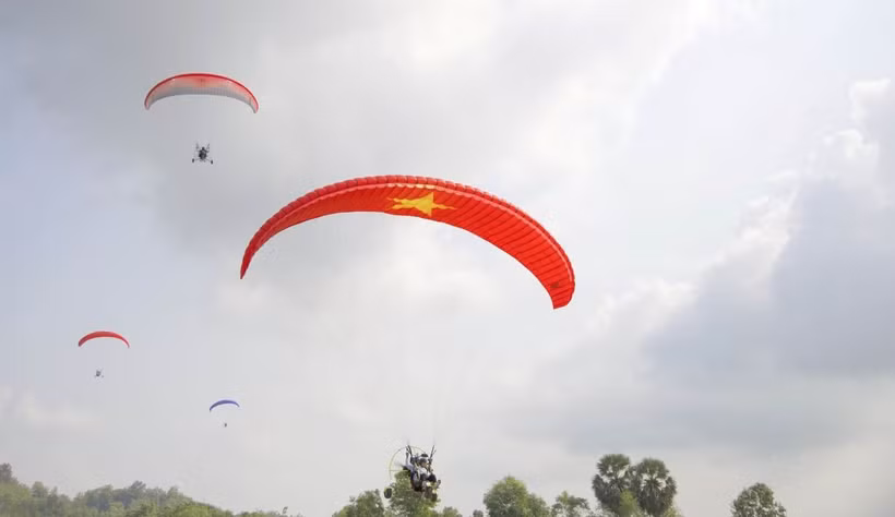 Các phi công thể hiện kỹ thuật điều khiển dù lượn trên bầu trời giữa cánh đồng thốt nốt. (Ảnh: Công Mạo/TTXVN)