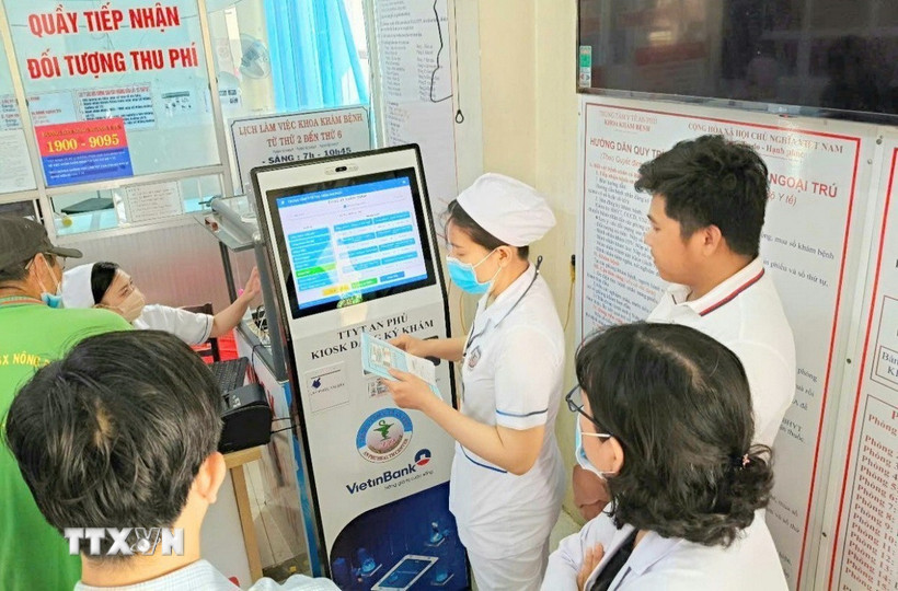 Cán bộ, nhân viên Trung tâm y tế An Phú, An Giang, hướng dẫn người dân đăng ký khám chữa bệnh bằng kiốt thông minh. (Ảnh: Công Mạo/TTXVN)