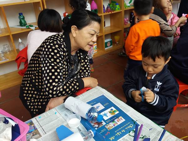 Một học sinh mầm non chăm chú cắt giấy để trang trí cho lọ hoa sẽ được làm từ vỏ chai nước ngọt. (Ảnh: PM/Vietnam+)