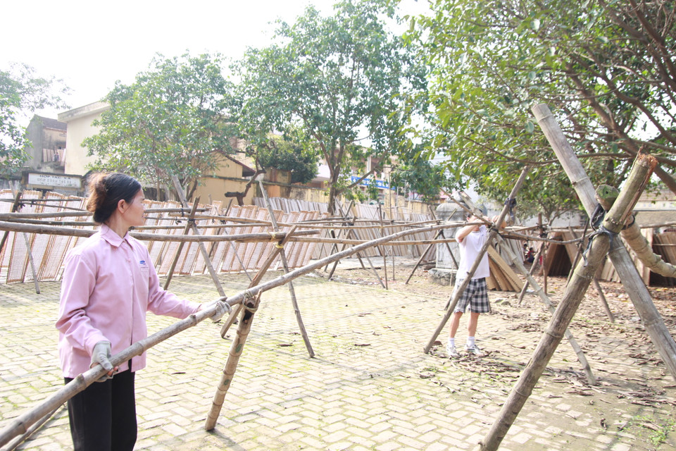 Người dân buộc khung để xếp bánh đa phơi ngay trong sân đình. Trước đây muốn làm được mẻ bánh đa rất tốn công sức, quạt lò tráng bánh, giã bột bằng tay… nhưng bây giờ, người làng đã áp dụng công nghệ vào sản xuất nên việc đã nhàn đi rất nhiều, một ngày có thể làm được nhiều mẻ, sản lượng tăng gấp đôi. (Ảnh: Mai Hiền/Vietnam+)