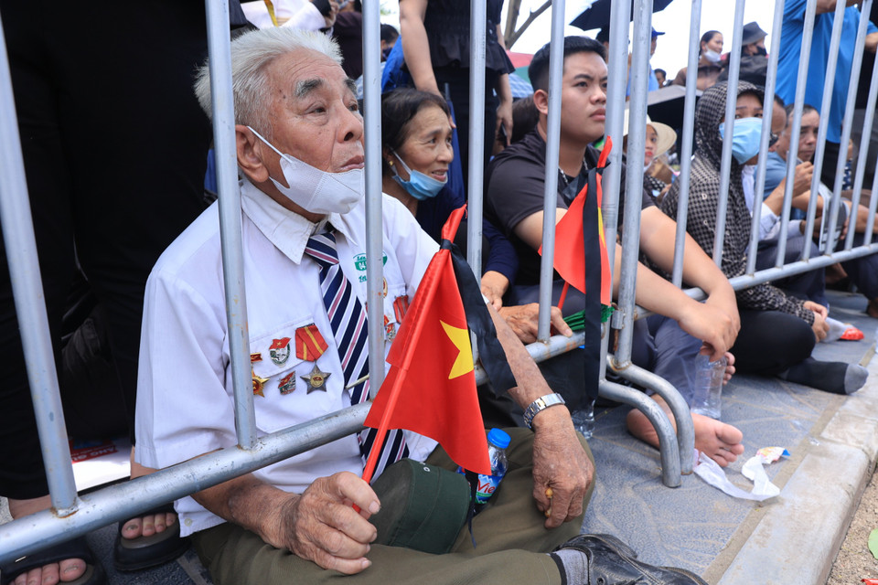 Một cựu chiến binh mang theo cờ rủ chờ đưa tiễn Tổng Bí thư. (Ảnh: Hoài Nam/Vietnam+)