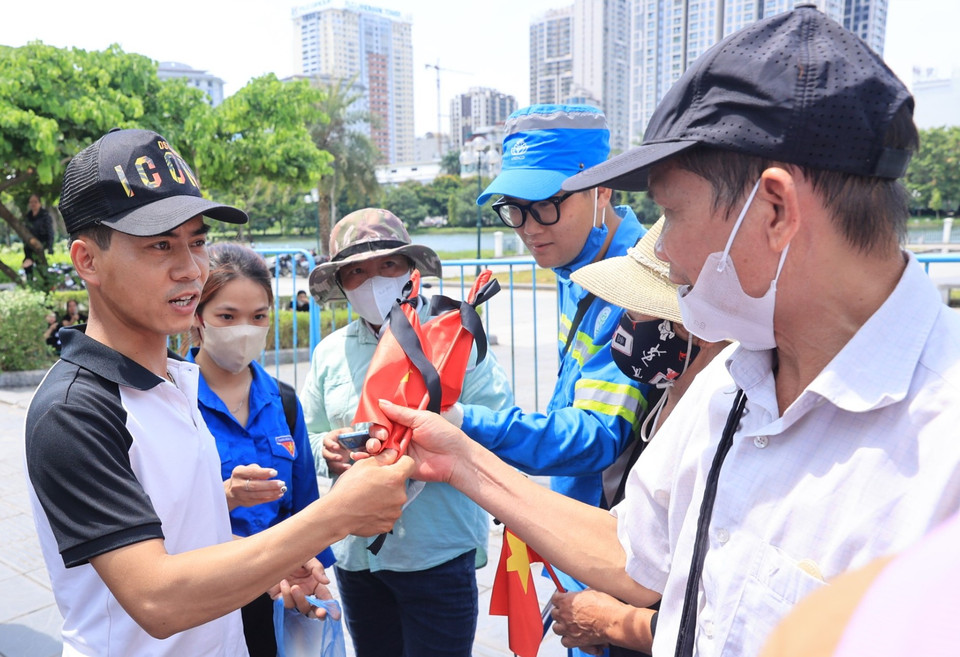 Người dân trao nhau những chiếc cờ rủ để cùng tiễn đưa Tổng Bí thư Nguyễn Phú Trọng. (Ảnh: Hoài Nam/Vietnam+)