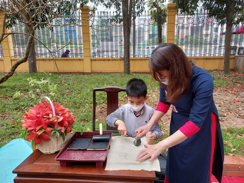 Cán bộ bảo tàng tận tình hướng dẫn các em in tranh trên giấy dó. (Ảnh: Minh Thu/Vietnam+)