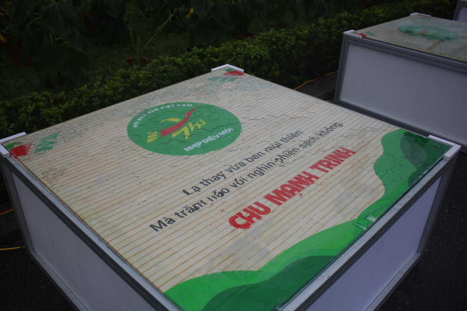 ''Thời tiết này không ảnh hưởng gì cả. 'Yêu nhau mấy núi cũng trèo cơ mà.' Chính thơ ca là thứ làm tâm hồn ta thanh thảnh,'' ông chia sẻ. Trời mưa phùn khiến các tờ in thơ và mặt kính ướt sũng nước. (Ảnh: Minh Anh/Vietnam+)