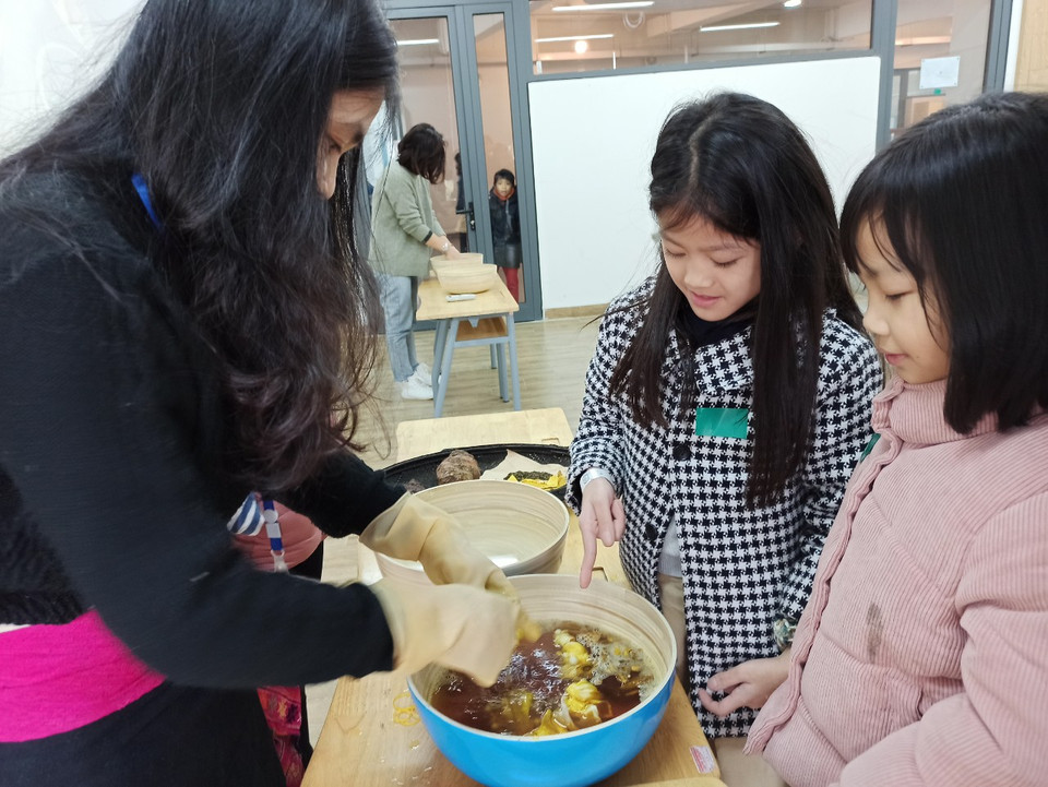 Chăm chú theo dõi nghệ nhân hướng dẫn cách nhuộm vải từ cây hoàng đằng. (Ảnh: PM/Vietnam+)