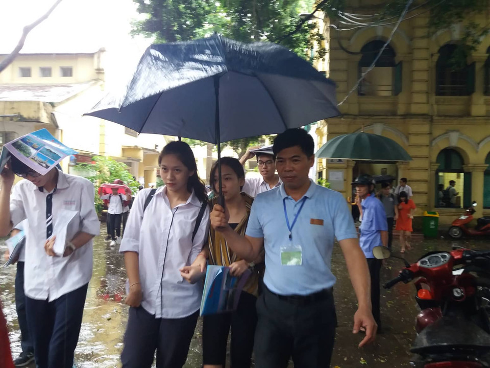 Hết giờ thi, cán bộ làm công tác thi tại trường Trung học phổ thông Việt Đức mang ô vào che mưa, đưa các thí sinh ra cổng trường. (PM/Vietnam+)