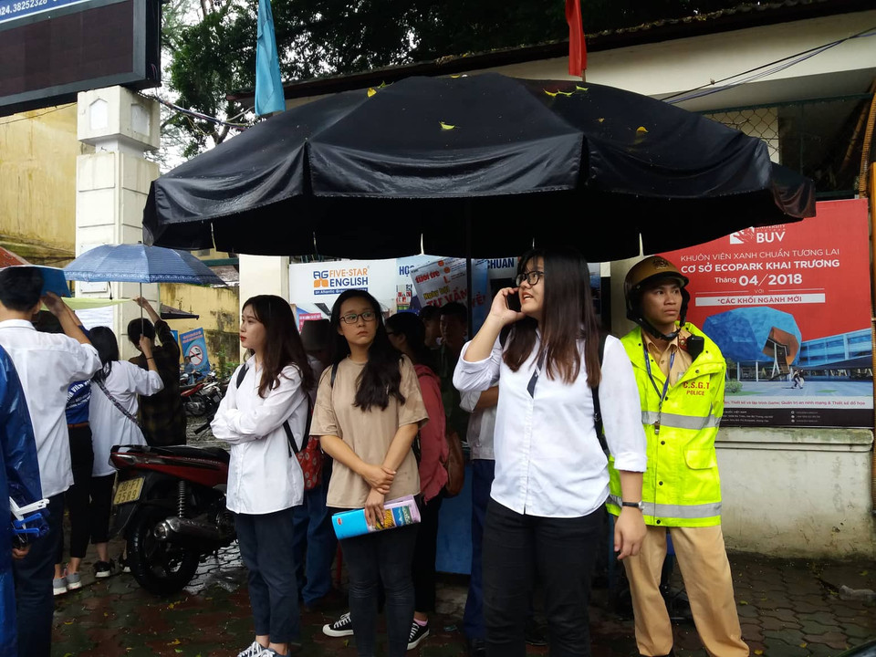 Thí sinh đứng đợi người đón, trời mưa làm cho việc tìm phụ huynh khó hơn. Thi sính phải gọi điện thoại cho mẹ để "định vị" nơi mình đứng đợi. (Ảnh: Phạm Mai/Vietnam+)