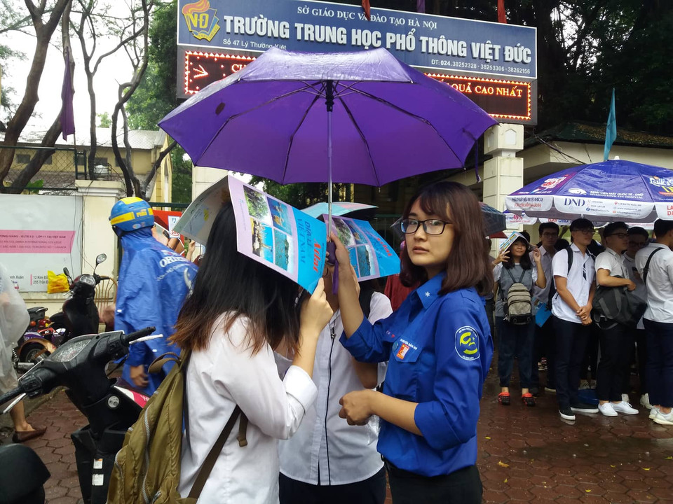 Tình nguyện viên che mưa cho thí sinh trong khi chờ bố mẹ đến đón. (Ảnh: Phạm Mai/Vietnam+)