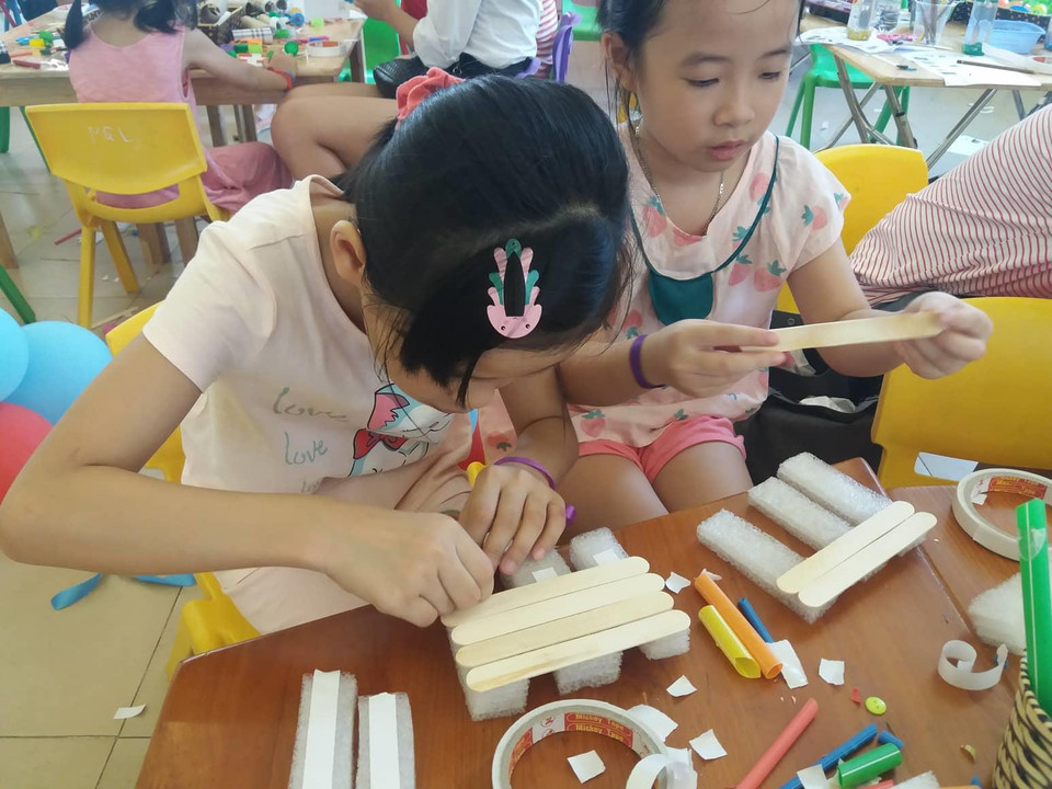 Minh Hồng (bên trái), 9 tuổi, lại thích thú với việc thiết kế chiếc bè nổi. Hồng cho biết, qua sự kiện, em phát hiện ra có thể chế tạo rất nhiều đồ chơi đơn giản từ vật liệu tưởng như bỏ đi. ‘Em sẽ làm thêm các đồ chơi, vật dụng khác bằng đồ tái chế khi về nhà,’ Hồng chia sẻ. (Ảnh: PV/Vietnam+)