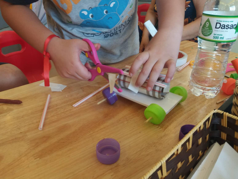 Cậu bé cẩn thận trang trí cho chiếc ô tô của mình bằng băng keo và ống hút. (Ảnh: PV/Vietnam+)