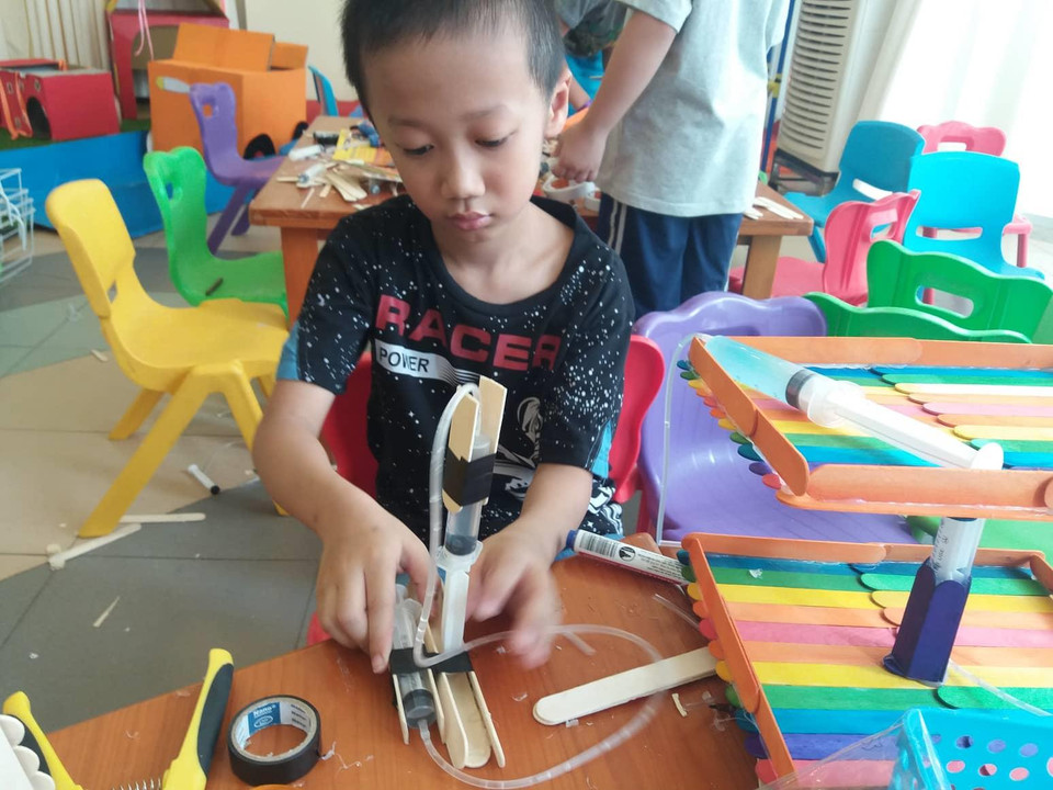 Với Đỗ Minh Hoàng, học sinh lớp 2 tiểu học Nam Thành Công, đây là lần đầu tiên em được tiếp xúc với giáo dục STEM vì ở trường em không có hoạt động này. Hoàng thích thú với trò chơi về áp lực nước, được làm từ xilanh và ống truyền dịch. (Ảnh: PV/Vietnam+)