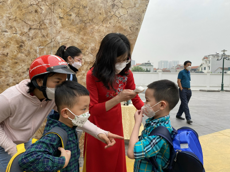 Tại đây, nhà trường bố trí người điều phối hỗ trợ đo nhiệt độ cho các con ngay tại cổng. Các bạn nhỏ này đến trường từ 7 giờ 30 phút. (Ảnh: Minh Anh/Vietnam+)