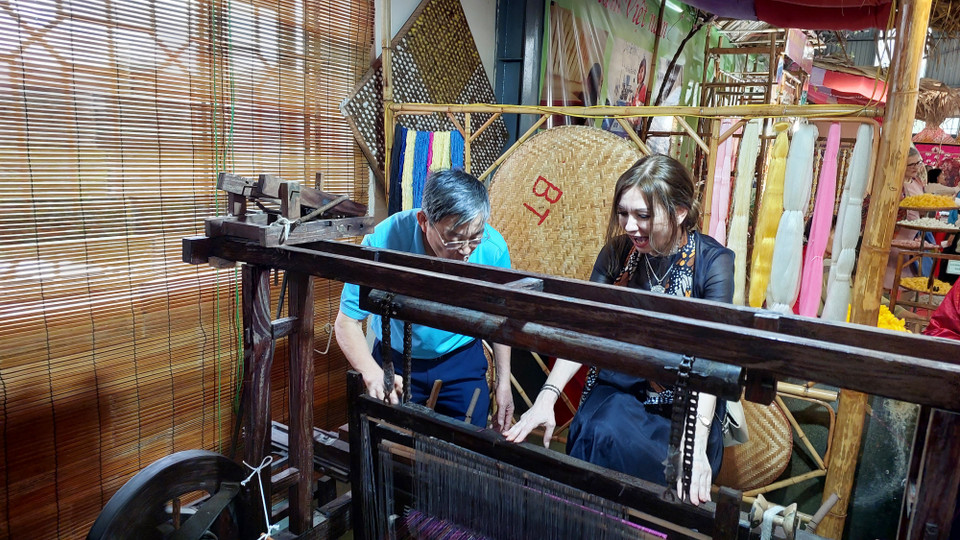 Nữ đại biểu thích thú khi được tự tay dệt lụa. (Ảnh: Minh Thu/Vietnam+)