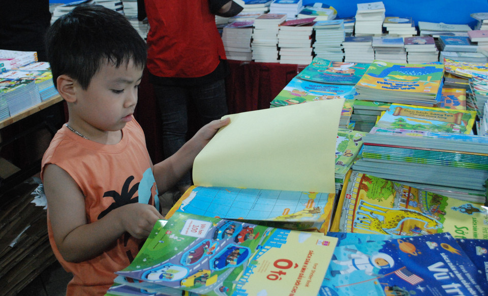 Một độc giả lứa tuổi mầm non say sưa lựa chọn cuốn sách yêu thích. (Ảnh: PV/Vietnam+)