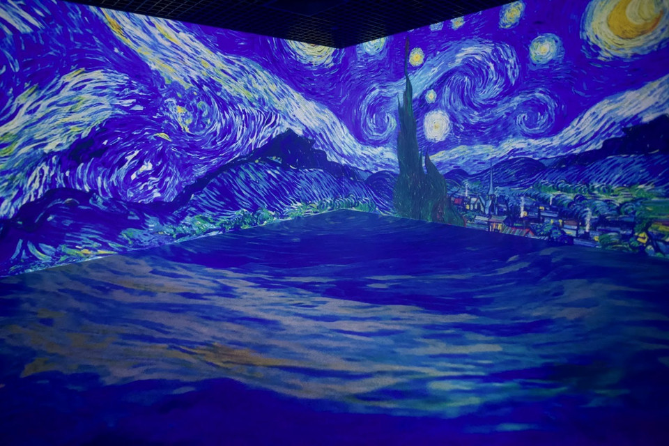 Trong tranh, ngôi làng Saint-Rémy nằm dưới bầu trời đầy sao, xa xa là dãy Alpilles, gần hơn là cây hoàng đàn vút cao. Thân cây vươn lên dường như ẩn chứa linh hồn họa sỹ, một con người khát khao hướng tới “vì sao” - những điều tốt đẹp ở đời. (Ảnh: Tuấn Anh/Vietnam+)