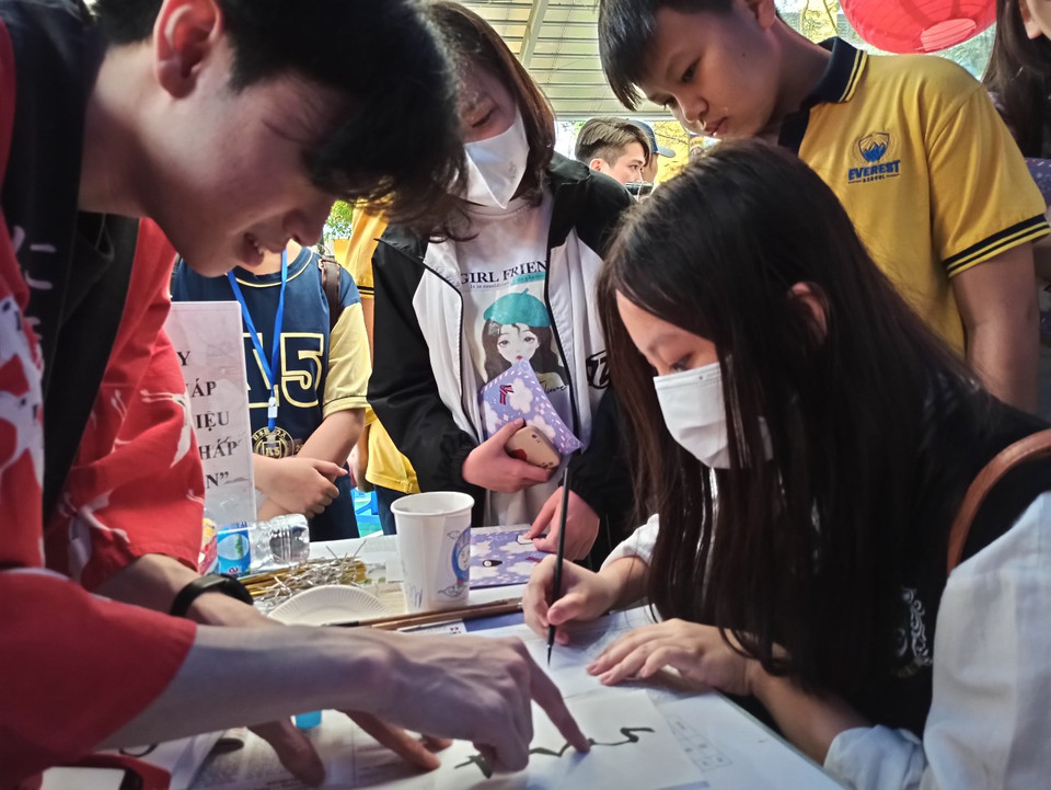 Trong khi đó những học sinh lớn hơn thích trải nghiệm viết thư pháp. (Ảnh: Phạm Mai/Vietnam+)