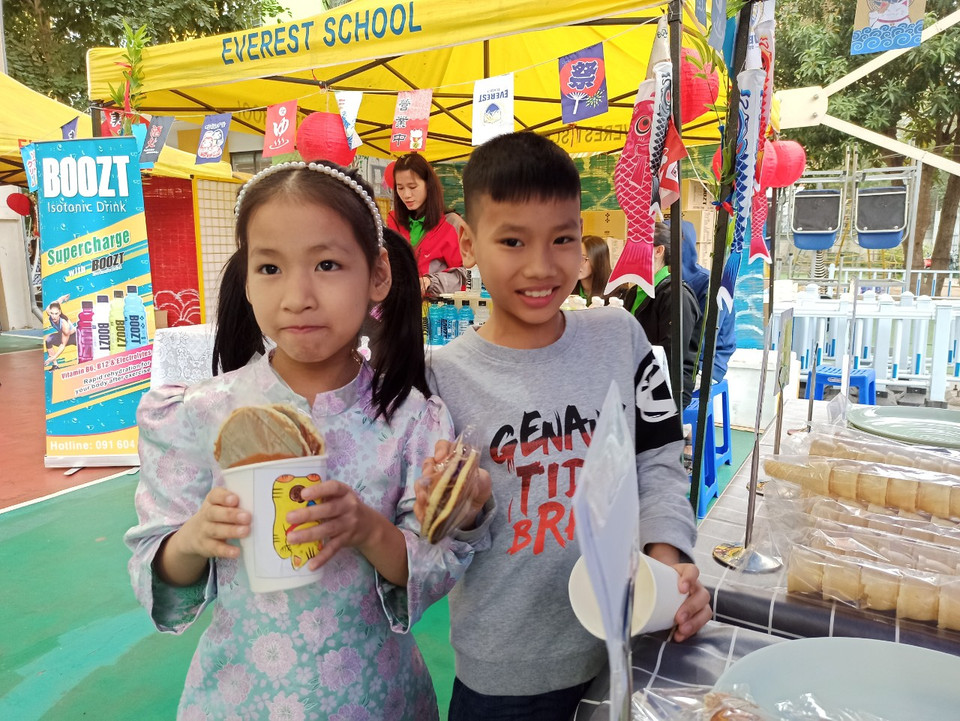 Dù trời lất phất mưa và nhà ở khá xa nhưng sáng nay, Nguyễn Thị Thanh Thư và Nguyễn An Phú (đều là học sinh Trường Tiểu học Lý Nam Đế) được mẹ đưa đến từ khá sớm. “Đây là bánh rán Doremon,” Thanh Thư cười tươi nói.(Ảnh: Phạm Mai/Vietnam).