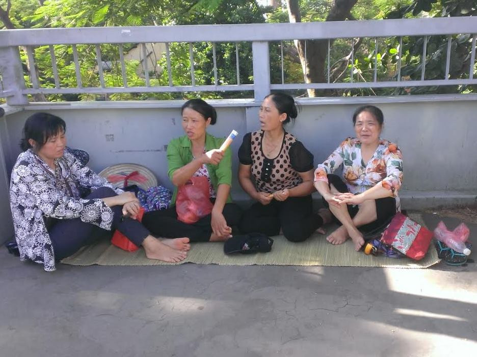 Ở một đầu của cầu vượt này, mấy phụ huynh mang sẵn chiếu trải để ngồi và trò chuyện trong lúc chờ đợi con thi. (Ảnh: Phạm Mai/Vietnam+)