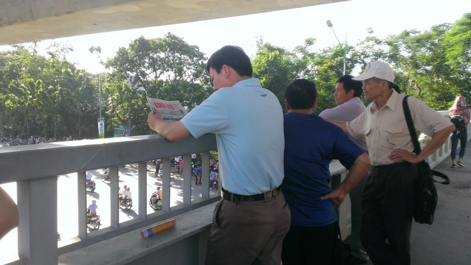 Phụ huynh vừa tránh nắng, vừa đọc báo và "ngắm" người qua lại từ trên cao. (Ảnh: Phạm Mai/Vietnam+)