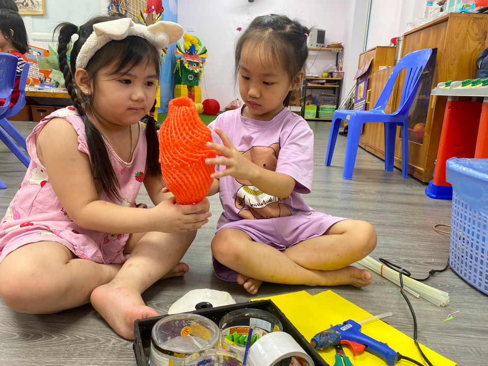 Các em bé phối hợp để cùng làm đèn lồng với nguyên liệu từ chai nhựa và vỏ bọc hoa quả. (Ảnh: NTCC)