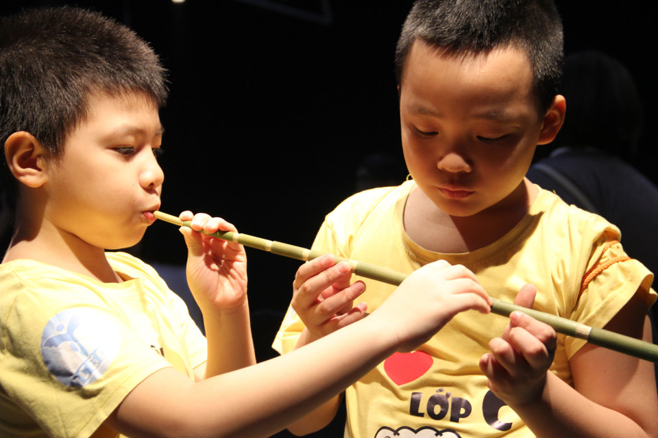 Khán giả nhí tập thổi sáo pi tơm. Nhạc cụ truyền thống của người Khơ Mú gồm nhiều loại, được phân chia theo các bộ như bộ khí (sáo dọc ba lỗ, sáo dọc bốn lỗ, sáo ngang, khèn bè…), bộ gảy (đàn trống, đàn môi…); bộ gõ (ống gõ, cồng chiêng…). (Ảnh: PV/Vietnam+)