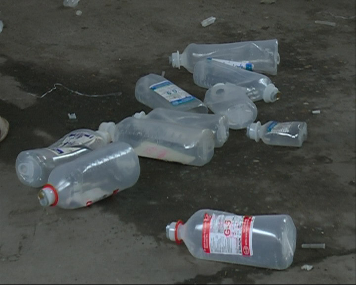 Những chai dịch truyền còn nước đổ thấm đẫm trên sàn của cơ sở tái chế. (Ảnh: Thùy Giang/Vietnam+)