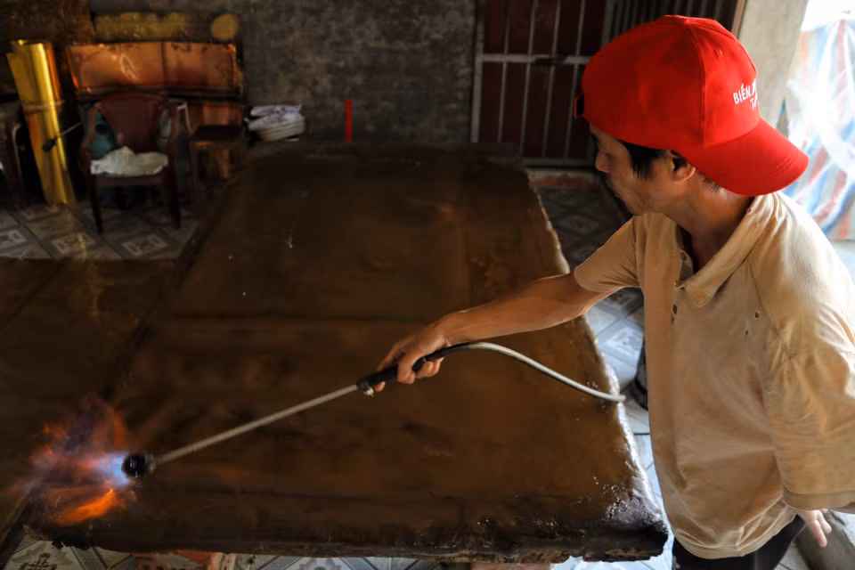 Tại làng nghề chạm bạc Đồng Xâm (xã Trà Giang, tỉnh Hưng Yên), một người thợ dùng đèn khò nung chảy lớp nhựa xi (hỗn hợp nhựa thông và đất mịn). Đây là công đoạn tạo lớp đế cố định, giúp miếng bạc có độ đàn hồi và vững chãi để chạm khắc hoa văn sắc nét mà không bị biến dạng. (Ảnh: Phương Anh/TTXVN phát)