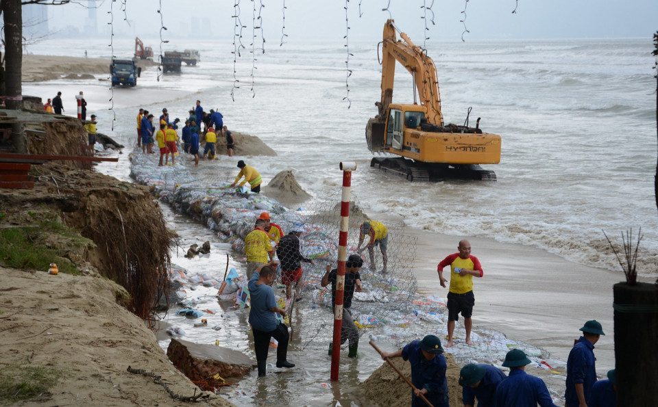 Hơn 200 nhân lực, cùng với một số máy múc, xe tải khẩn trương làm kè tạm chắn sóng, ngăn không cho sóng biển tiếp tục đánh vào bờ biển Mỹ Khê. (Ảnh: Văn Dũng/TTXVN)