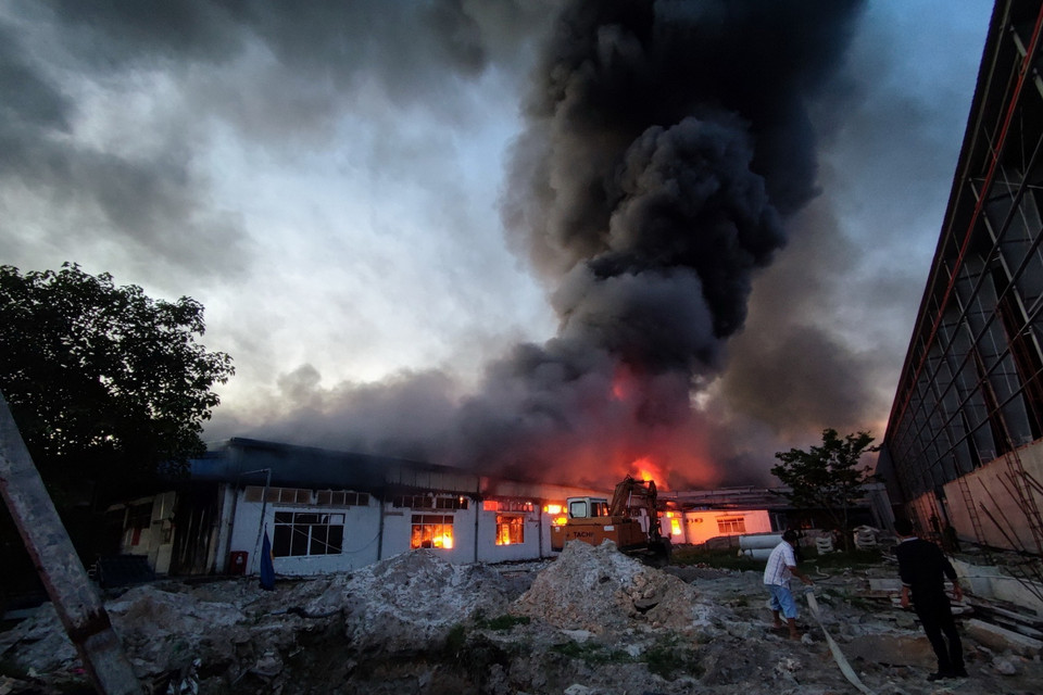 Trong kho chứa nhiều nguyên vật liệu dễ cháy như vải, cao su... nên ngọn lửa vẫn bốc cao và lan rộng… (Ảnh: TTXVN phát)