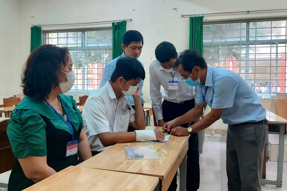 Các giám thị hỗ trợ gắn thiết bị ghi âm giám sát quá trình thi môn Ngữ Văn của thí sinh Tạ Quốc Hùng tại điểm thi Trường THPT Bùi Hữu Nghĩa, quận Bình Thủy, thành phố Cần Thơ bị tai nạn gãy tay nên không thể làm bài thi môn Ngữ Văn. (Ảnh: Hồng Thái/TTXVN)