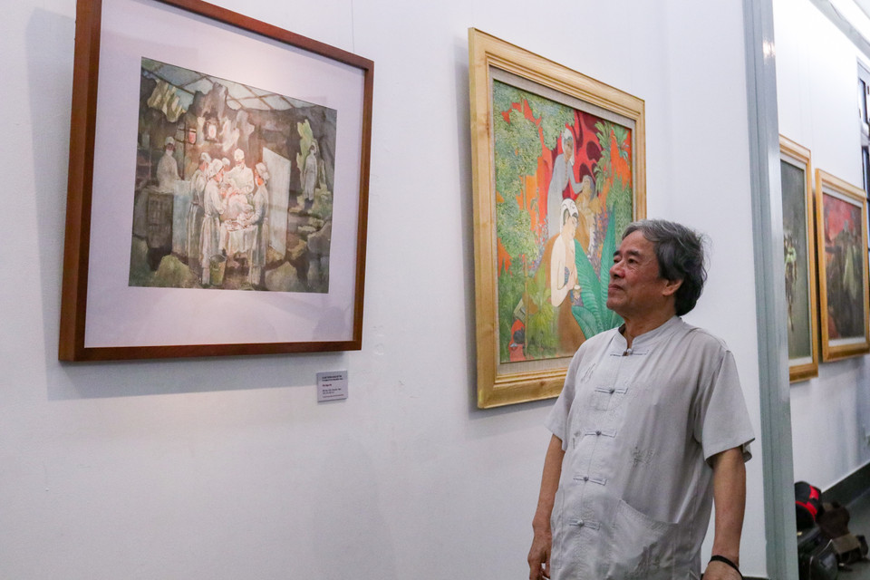 Họa sỹ Trần Ngọc Hải là tác giả của bức tranh “Ca mổ trong hang sơ tán.” Bức tranh được ra đời khắc họa lại chính khoảng thời gian mà ông - là người bác sỹ trên chiến trường đang thực hiện những ca mổ cho những chiến sỹ bị thương.“Có những đêm tôi phải thực hiện tới 45 ca mổ từ sáng tới đêm buồn ngủ đến díp cả mắt. Tuy nhiên, để giành giật lại sự sống cho những người chiến sỹ đã anh dũng chiến đấu nên tôi vẫn tiếp tục cố gắng…,” ông Hải chia sẻ. (Ảnh: Minh Hiếu/Vietnam+)