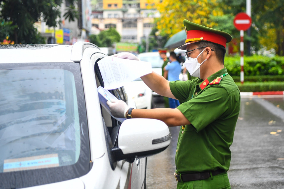 Ngoài việc kiểm tra giấy đi đường của từng trường hợp, lực lượng trực chốt đã nhắc nhở người dân bổ sung đầy đủ lịch trực, lịch làm việc, văn bản phân công nhiệm vụ trong giấy đi đường theo quy định mới. (Ảnh: Minh Sơn/Vietnam+)