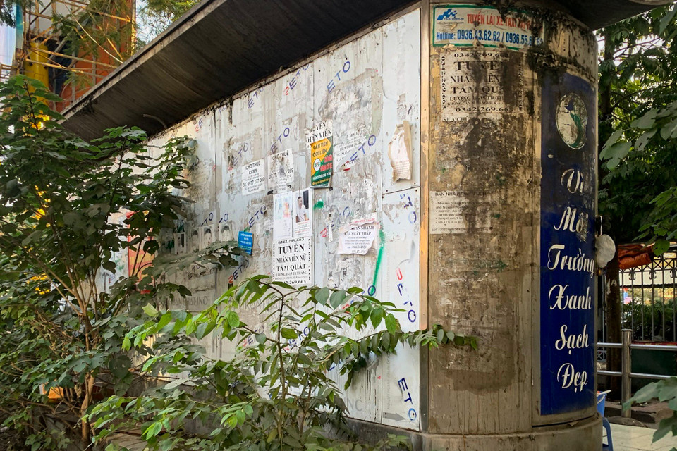 Nhà vệ sinh công cộng trên đường Nguyễn Hoàng (Nam Từ Liêm, Hà Nội) trong cảnh hoang tàn, cỏ cây mọc um tùm và mang trên mình chi chít những tờ quảng cáo. (Ảnh: Hoài Nam/Vietnam+)