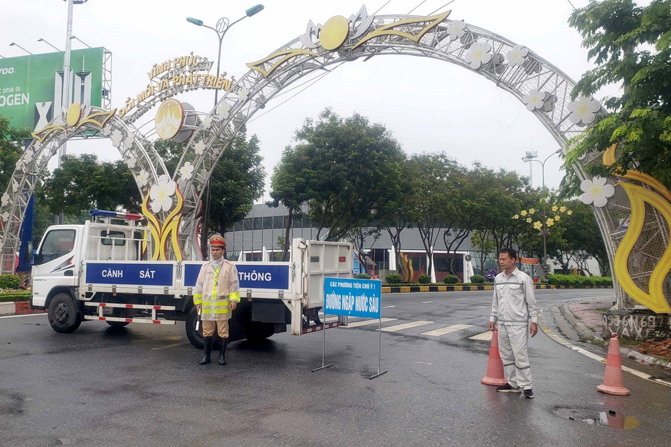 Cảnh sát giao thông phân luồng cho các phương tiện tham gia giao thông tránh đi vào các vùng bị ngập nước tại thành phố Vĩnh Yên. (Ảnh: Hoàng Hùng/TTXVN)