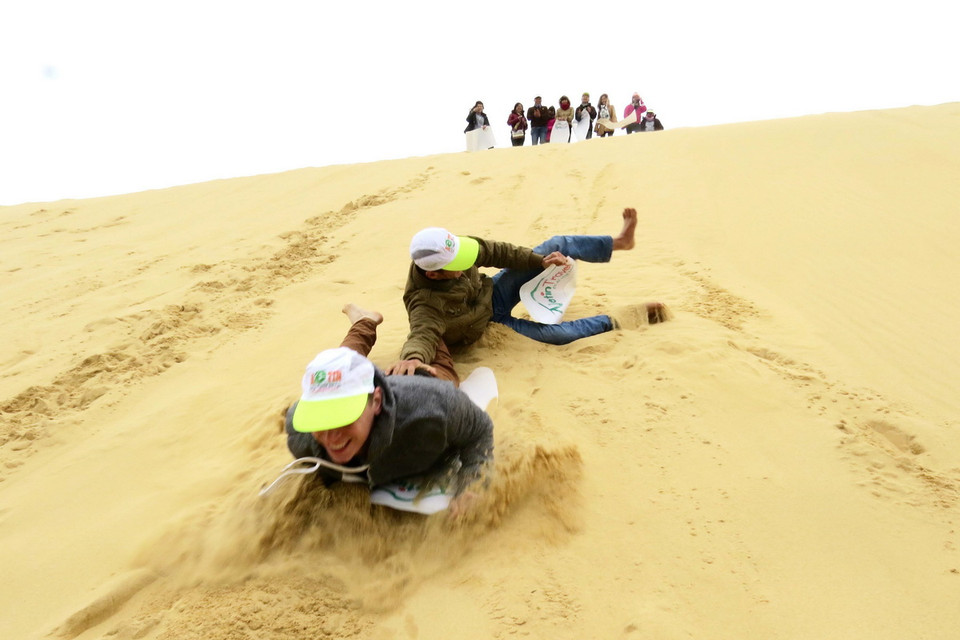 Du khách thích thú tham gia trò chơi trượt cát. (Ảnh: Mạnh Thành/TTXVN)