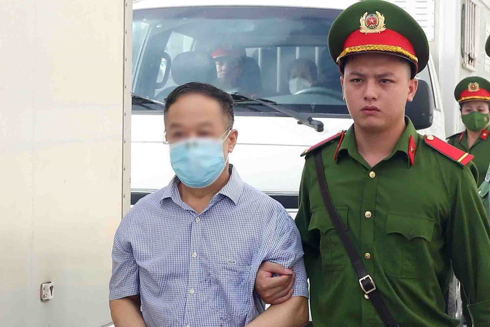 Lực lượng chức năng dẫn giải bị cáo Trần Văn Dự, cựu Phó Cục trưởng Cục Quản lý Xuất Nhập cảnh, Bộ Công an, tới phiên tòa xét xử. (Ảnh: Phạm Kiên/TTXVN)