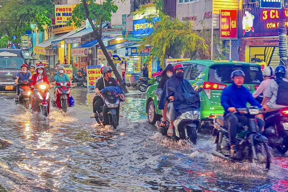 Các phương tiện vất vả di chuyển giữa dòng nước ngập trên đường D5 (quận Bình Thạnh). (Ảnh: Hồng Giang/TTXVN)