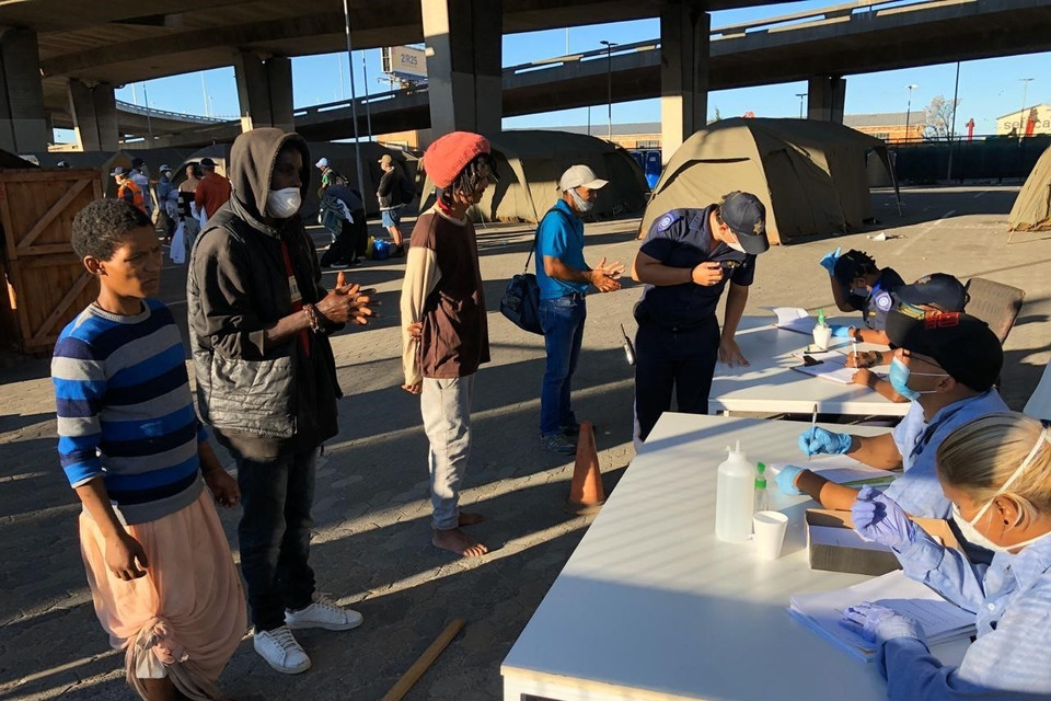 Để ngăn đà lây lan của dịch COVID-19, Chính phủ Nam Phi tiến hành nhiều biện pháp giúp người vô gia cư có được mái nhà tạm cùng những bữa ăn miễn phí trong 21 ngày nước này áp dụng lệnh phong tỏa trên quy mô toàn quốc. Lực lượng chức năng ghi chép thông tin cá nhân của người vô gia cư trước khi cho họ vào khu nhà tạm. (Ảnh: Phi Hùng/TTXVN)