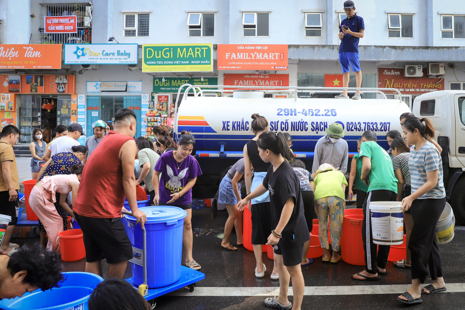 Cư dân mang theo xô, chậu, thùng nhựa và bất kể vật dụng gì có thể chứa được nước đến sảnh chung cư, xếp hàng đợi đến lượt nhận nước sạch về sinh hoạt. (Ảnh: Hoài Nam/Vietnam+)