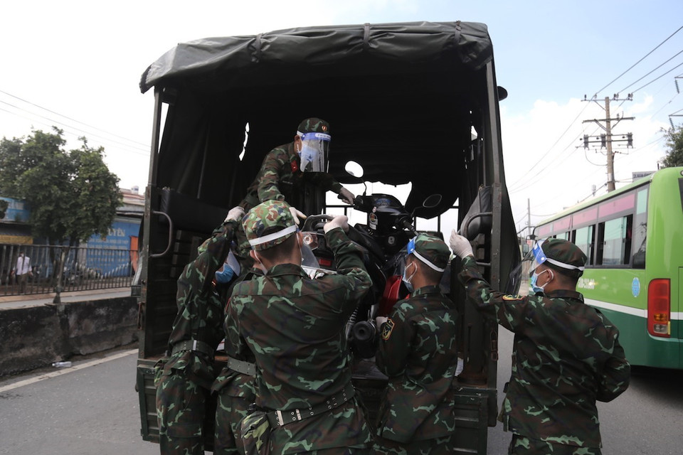 Lực lượng kiểm soát quân sự vận chuyển xe máy cho người dân lên xe ôtô chở về quê. (Ảnh: TTXVN phát)