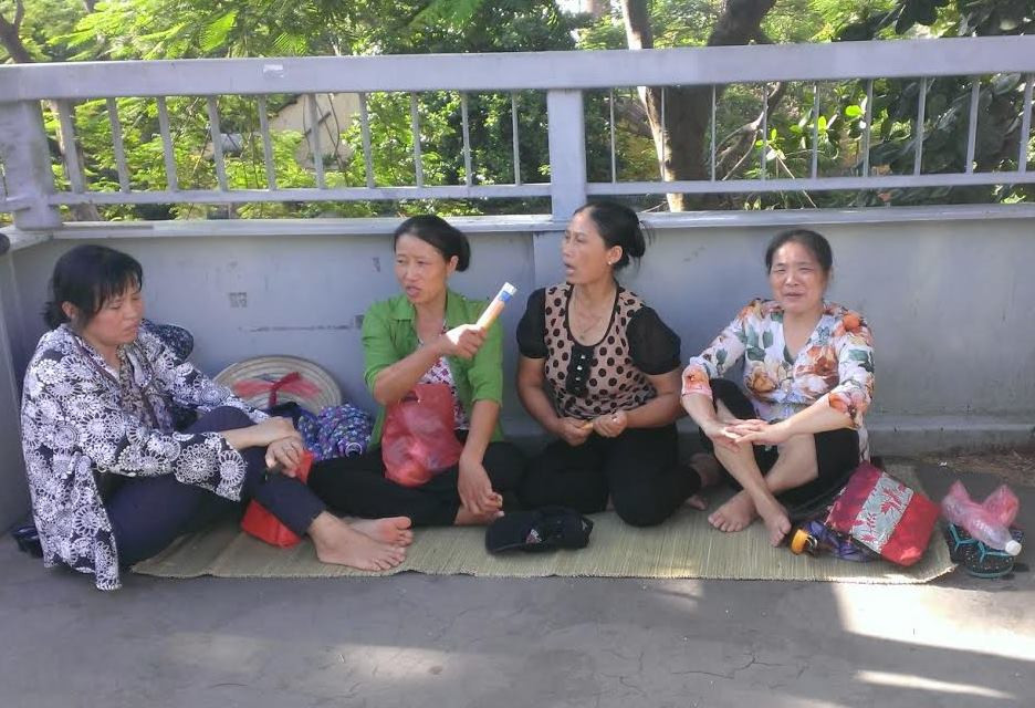 Ở một đầu của cầu vượt này, mấy phụ huynh mang sẵn chiếu trải để ngồi và trò chuyện trong lúc chờ đợi con thi. (Ảnh: Phạm Mai/Vietnam+)