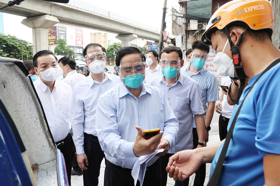 Thủ tướng Phạm Minh Chính kiểm tra giấy phép đi đường và khai báo y tế của một nhân viên giao hàng trên địa bàn quận Thanh Xuân. (Ảnh: Dương Giang/TTXVN)