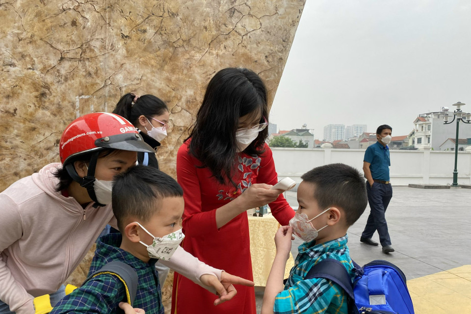 Tại đây, nhà trường bố trí người điều phối hỗ trợ đo nhiệt độ cho các con ngay tại cổng. Các bạn nhỏ này đến trường từ 7 giờ 30 phút. (Ảnh: Minh Anh/Vietnam+)