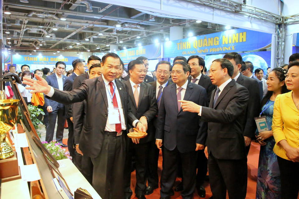 Thủ tướng Phạm Minh Chính nghe giới thiệu về các sản phẩm nông nghiệp, thủ công, mỹ nghệ của các tỉnh Đồng bằng sông Hồng. (Ảnh: Dương Giang/TTXVN)