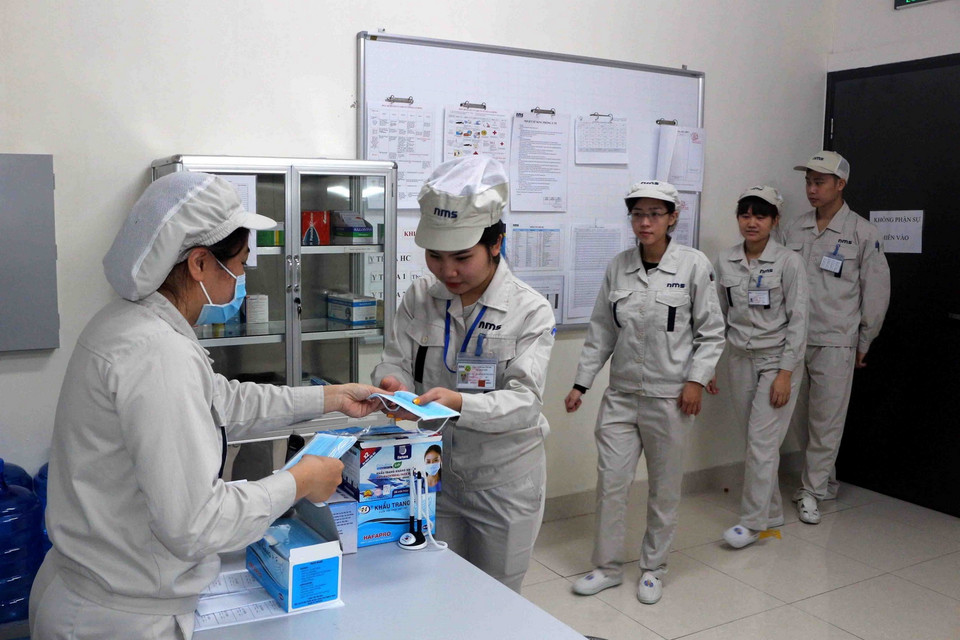 Công nhân Công ty TNHH NMS Việt Nam (Hà Nam) được phát mỗi ngày 1 chiếc khẩu trang y tế trước khi vào làm. (Ảnh: Đại Nghĩa/TTXVN)