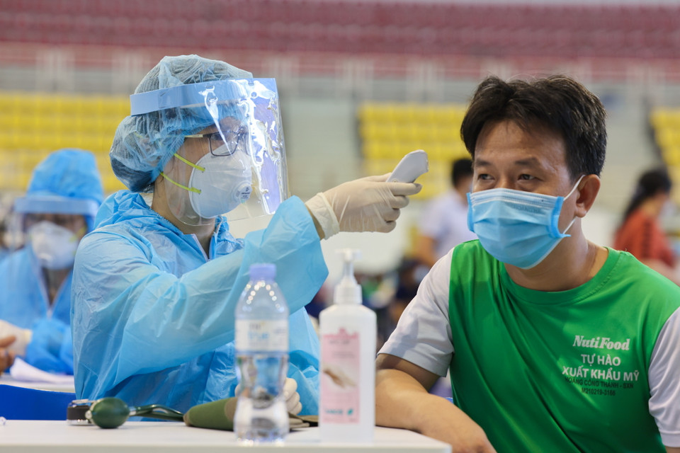 Nhân viên y tế đo thân nhiệt cho những người đến tiêm. (Ảnh: Hải An/Vietnam+)